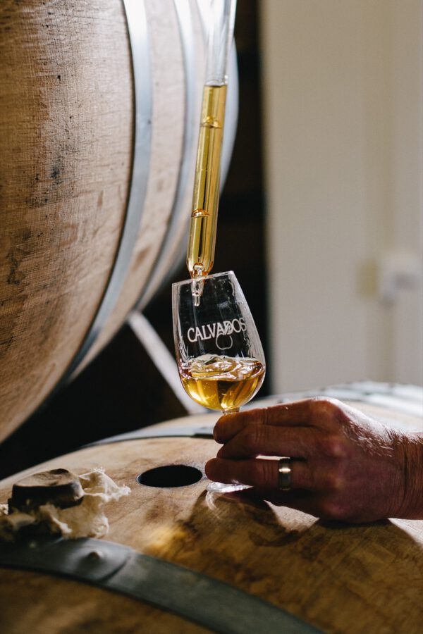 Verre de Calvados en cours de remplissage, posé sur un fût en bois, dans une cidrerie artisanale.