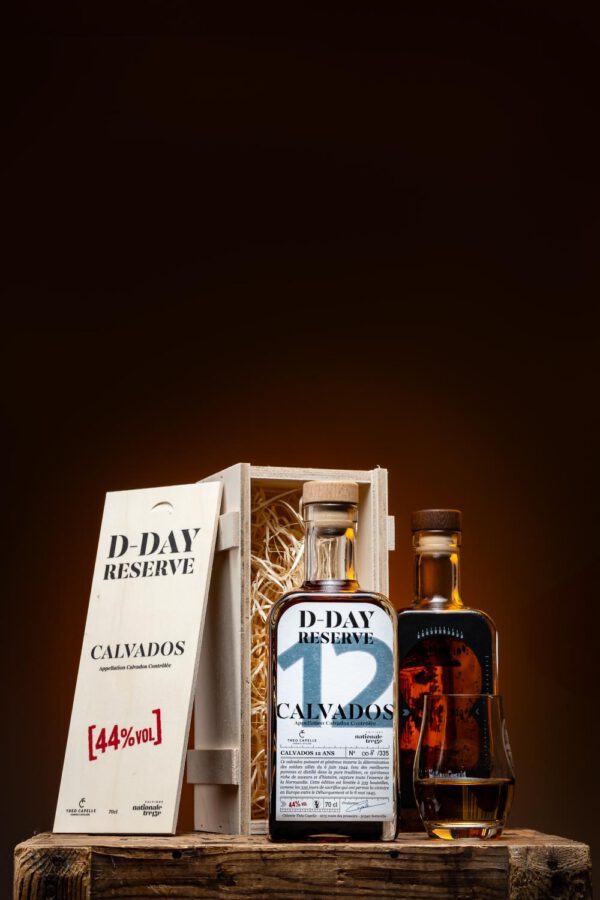 Bouteilles de Calvados D-DAY Réserve 12 ans dans un coffret en bois, accompagnées d'un verre, sur fond sombre.