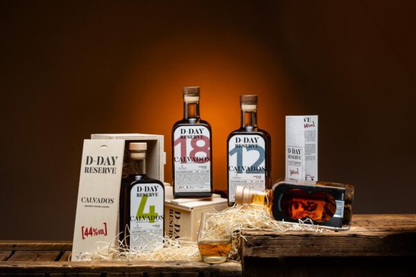 Assortiment de Calvados D-Day Réserve, mettant en avant différentes bouteilles et un verre sur une table en bois.