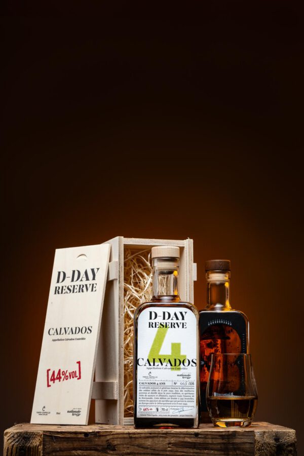 Bouteille de Calvados D-Day Réserve 4 ans dans son coffret en bois, accompagnée d'un verre, sur fond sombre.