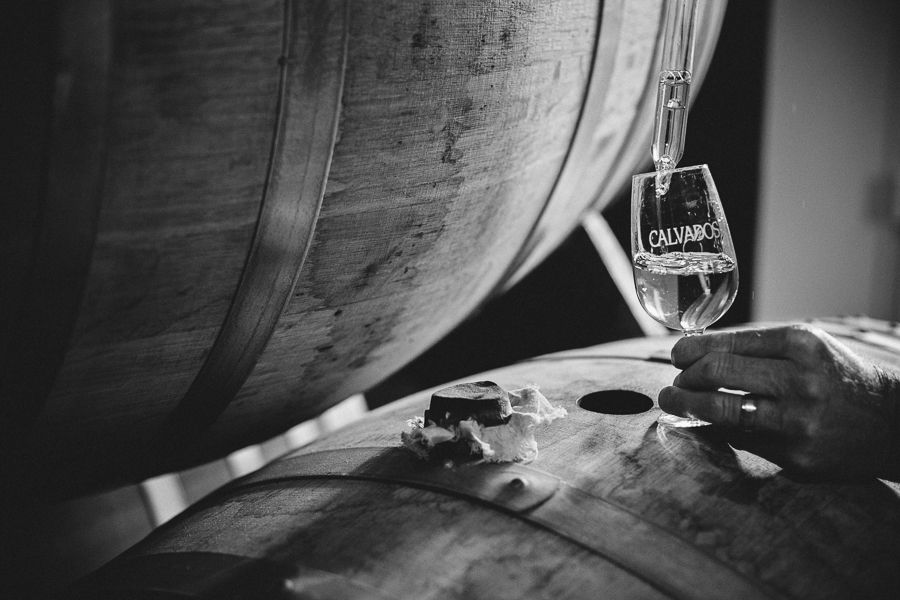Un verre de Calvados est rempli depuis un fût en bois dans une distillerie artisanale.