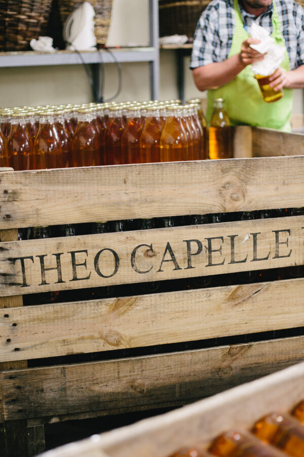 Une caisse de la cidrerie Théo Capelle avec des bouteilles de jus de pomme acidulé en arrière-plan.