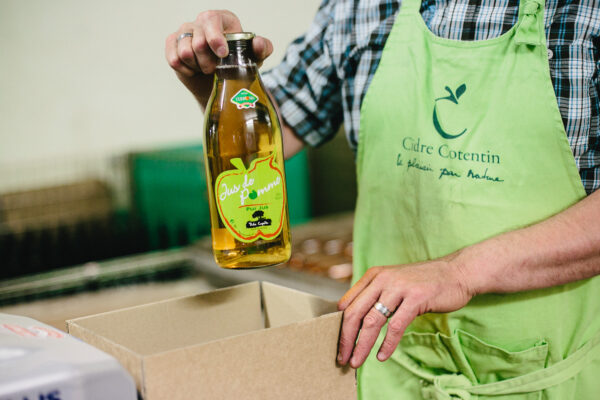 Bouteille de jus de pomme biologique présentée par un homme en tablier, prête à être placée dans une boîte.