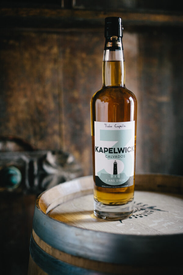 Bouteille de Calvados AOC 3 ans d'âge, Cidrerie-Distillerie Théo Capelle, posée sur un fût en bois.