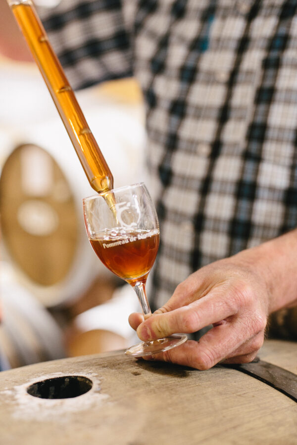 Un verre de Pommeau de Normandie étant rempli avec un tube à essai en bois, posé sur un baril en chêne.