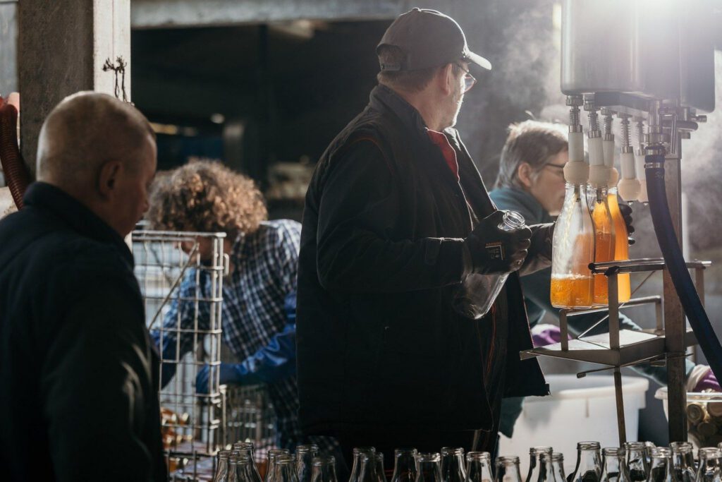 Travailleurs de la Cidrerie-Distillerie Théo Capelle en train de remplir des bouteilles de cidre dans un environnement artisanal.
