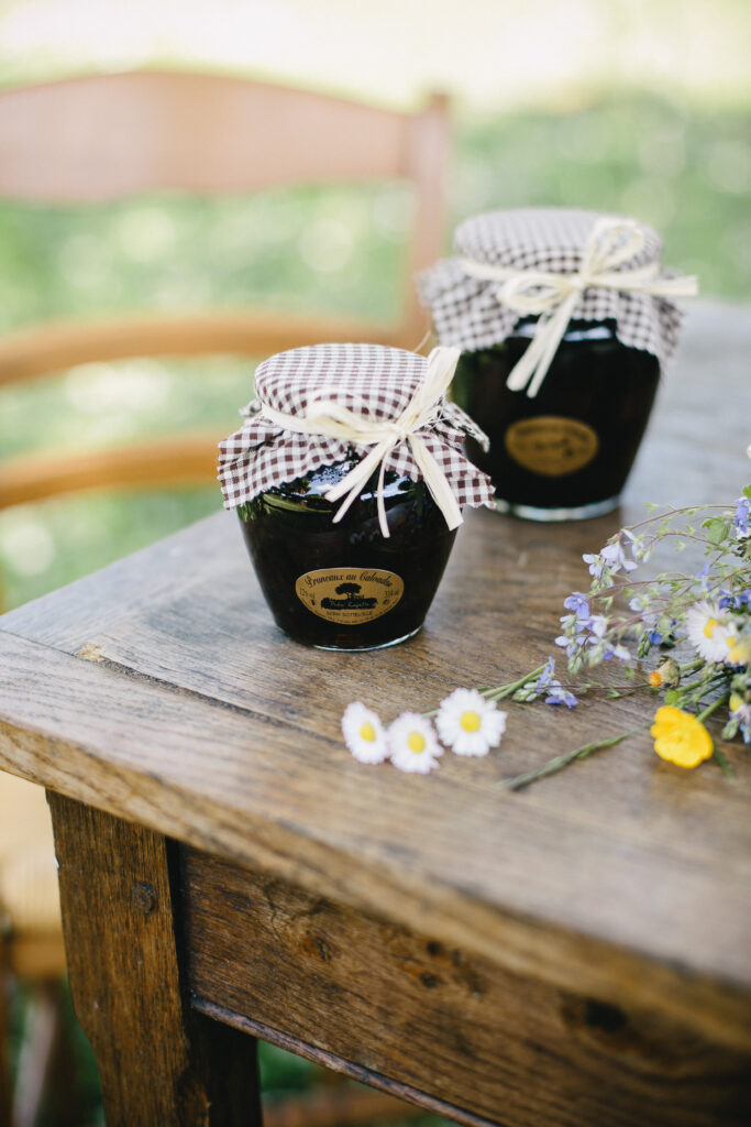 Bocal de pruneaux au calvados de 580 ml, sur une table en bois avec des fleurs.