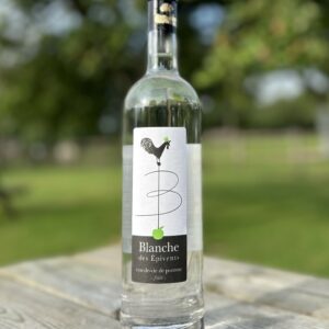 Bouteille de Blanche des Epivents, eau-de-vie de pomme de la cidrerie Théo Capelle, sur une table en bois en extérieur.