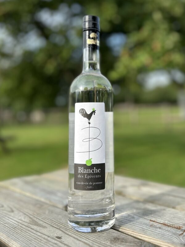 Bouteille de Blanche des Epivents, eau-de-vie de pomme de la cidrerie Théo Capelle, sur une table en bois en extérieur.