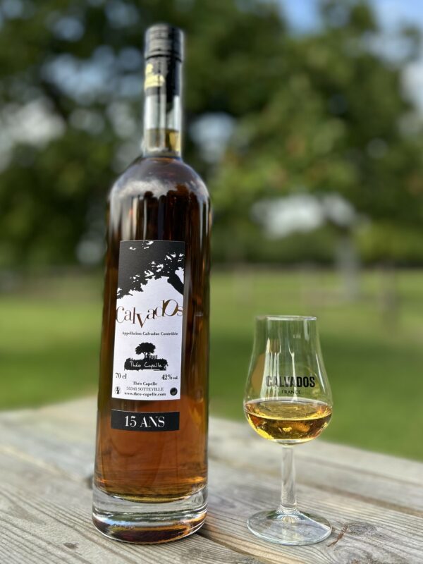 Bouteille de Calvados AOC 15 ans de 70 cl, accompagnée d'un verre, sur une table en bois en extérieur.