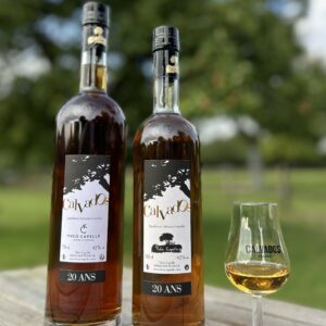 Deux bouteilles de Calvados AOC 20 ans, accompagnées d'un verre et d'un arrière-plan verdoyant, représentant la Cidrerie Théo Capelle.