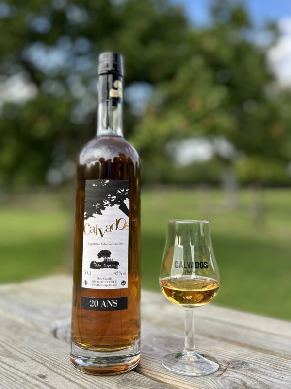 Bouteille de Calvados AOC 20 ans et verre, sur une table en bois en pleine nature.
