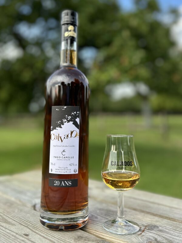 Bouteille de Calvados AOC 20 ans et verre, sur une table en bois, en arrière-plan, verger flou.