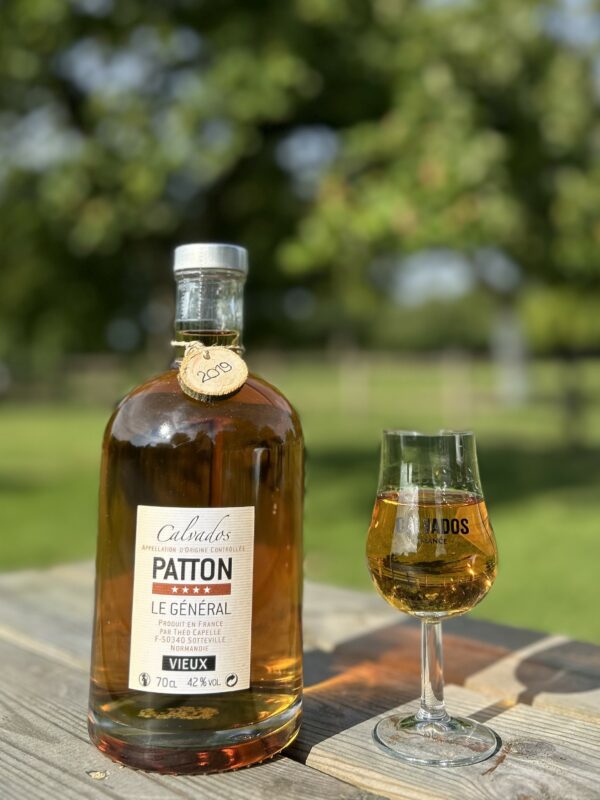 Bouteille de Calvados Patton 70 cl, accompagnée d'un verre, sur une table en bois avec un fond nature.