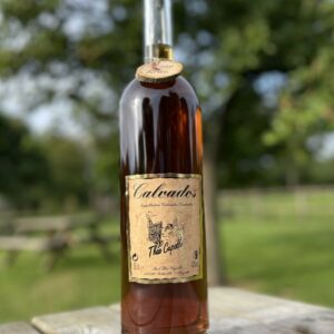 Bouteille de Calvados de la Cidrerie-Distillerie Théo Capelle, sur une table en bois, avec un fond d'arbres.