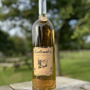 Bouteille de Calvados de la Cidrerie-Distillerie Théo Capelle, artisanale et AOP, sur fond verdoyant.