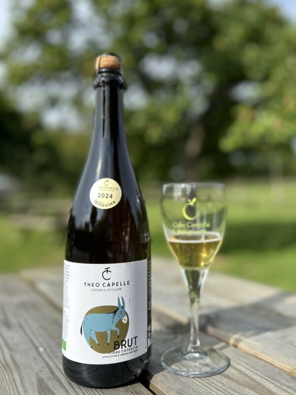 Bouteille de cidre AOP Cotentin Brut 2024, accompagnée d'un verre, sur une table en bois en plein air.
