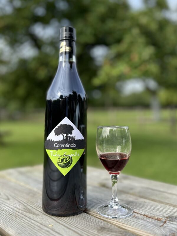 Bouteille de Cotentinoix 70 cl de la cidrerie Théo Capelle, accompagnée d'un verre sur une table en bois, en plein air.