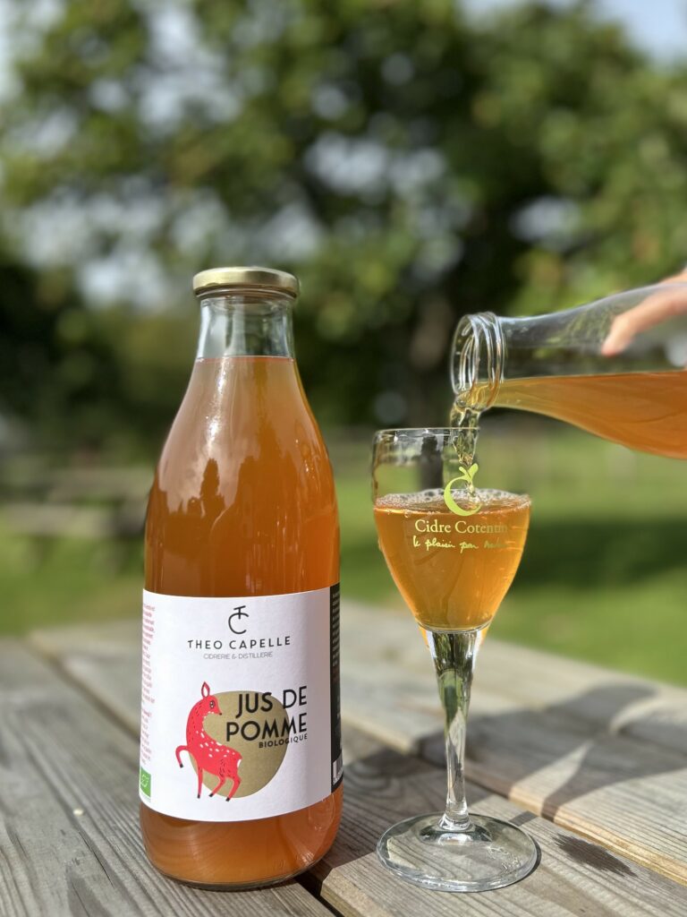 Bouteille de jus de pomme biologique de 1 litre de la cidrerie Théo Capelle, servie dans un verre, en plein air.