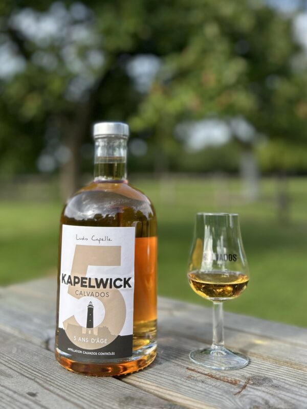 Bouteille de Calvados 5 ans d'âge, accompagnée d'un verre, sur une table en bois avec un arrière-plan verdoyant.