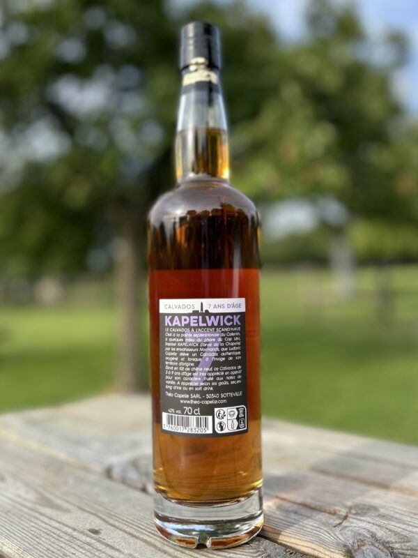Bouteille de Calvados KAPELWICK 7 ans d'âge, fond flou avec un paysage vert en arrière-plan.