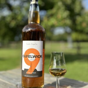 Bouteille de Calvados KAPELWICK 9 ans et un verre sur une table en bois, entourée de verdure.