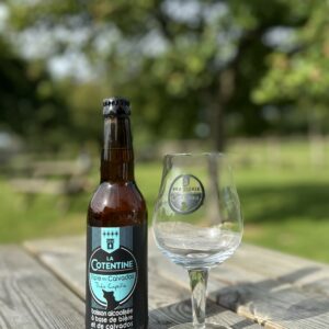 Bouteille de bière "La Cotentine" de 33cl, accompagnée d'un verre, sur une table en bois, en pleine nature.