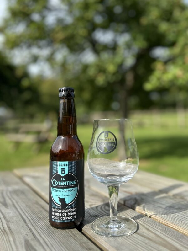 Bouteille de bière "La Cotentine" de 33cl, accompagnée d'un verre, sur une table en bois, en pleine nature.