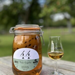 Bocal de liqueur 44 Quarante-Quatre de Théo Capelle avec un verre de Calvados sur une table en bois, entouré de verdure.