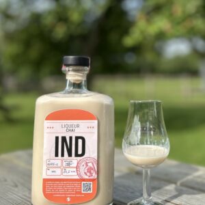 Bouteille de liqueur Chai IND avec un verre sur une table en bois, en arrière-plan, un jardin verdoyant.