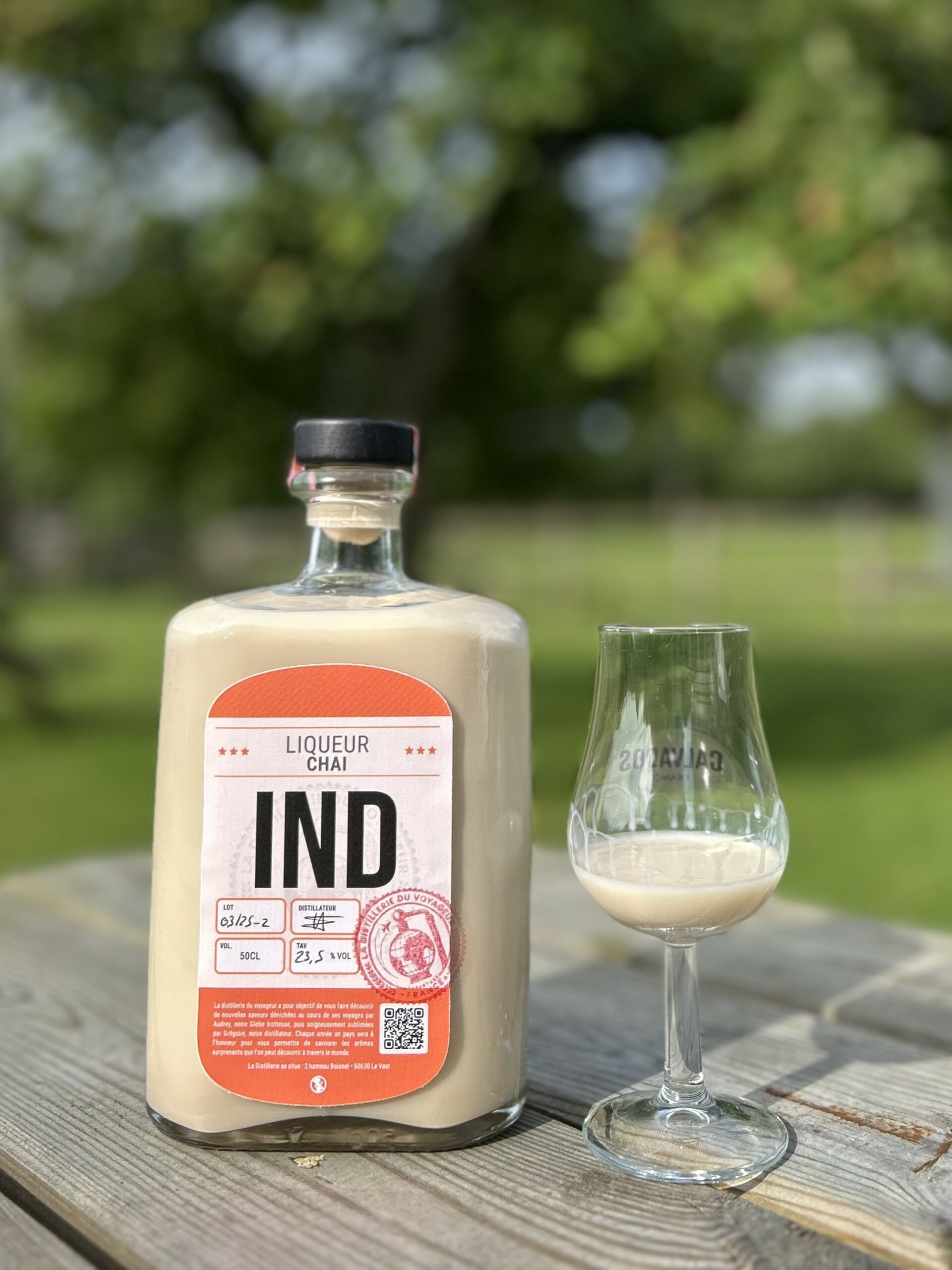 Bouteille de liqueur Chai IND avec un verre sur une table en bois, en arrière-plan, un jardin verdoyant.