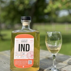 Bouteille de liqueur Shikanji IND et un verre sur une table en bois, en plein air.