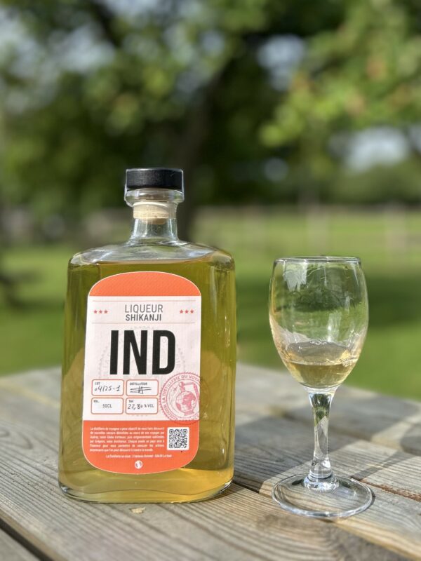 Bouteille de liqueur Shikanji IND et un verre sur une table en bois, en plein air.
