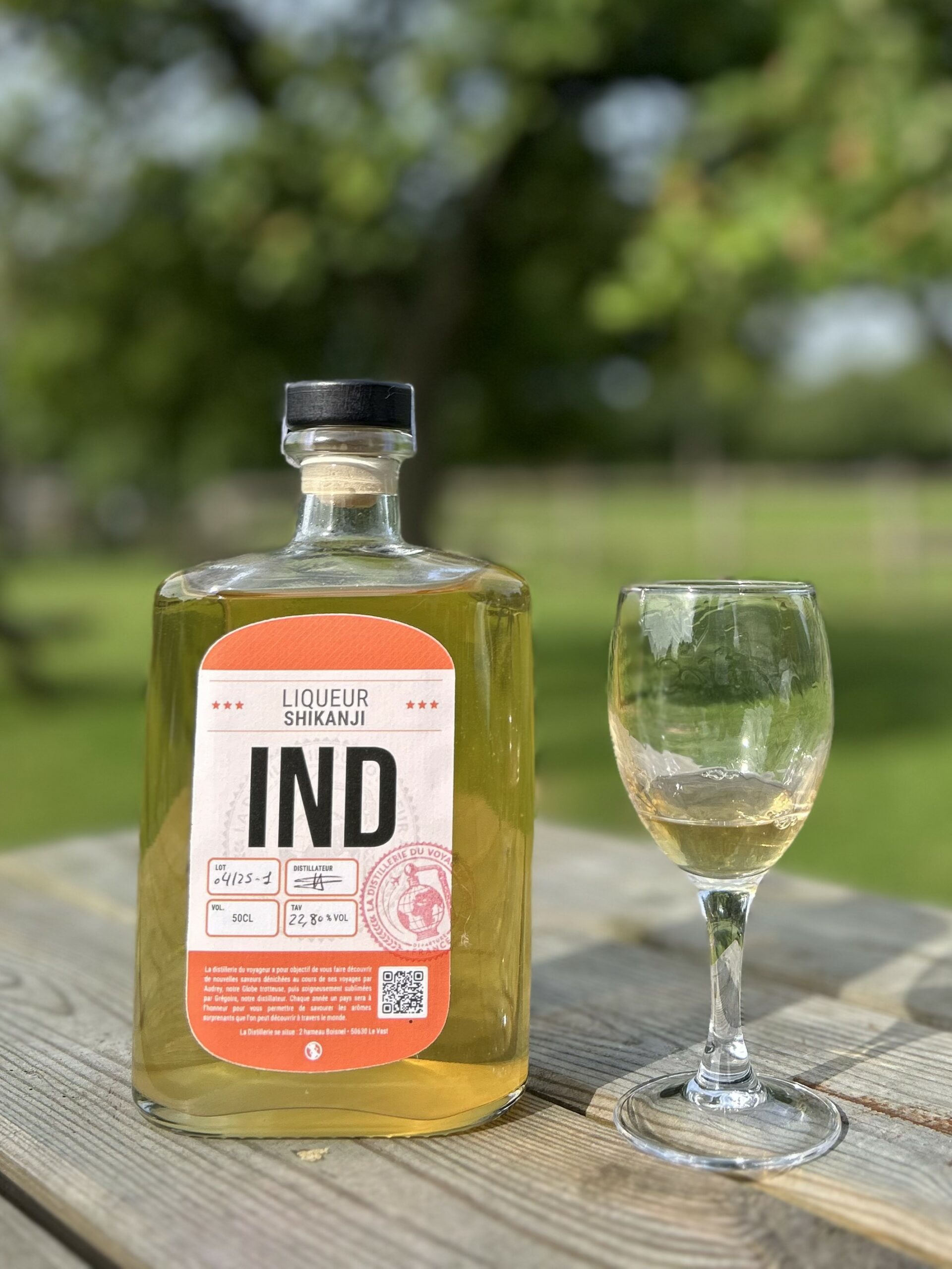 Bouteille de liqueur Shikanji IND et un verre sur une table en bois, en plein air.