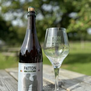 Bouteille de bière belge "Le Général" et un verre sur une table en bois, avec un arrière-plan naturel.