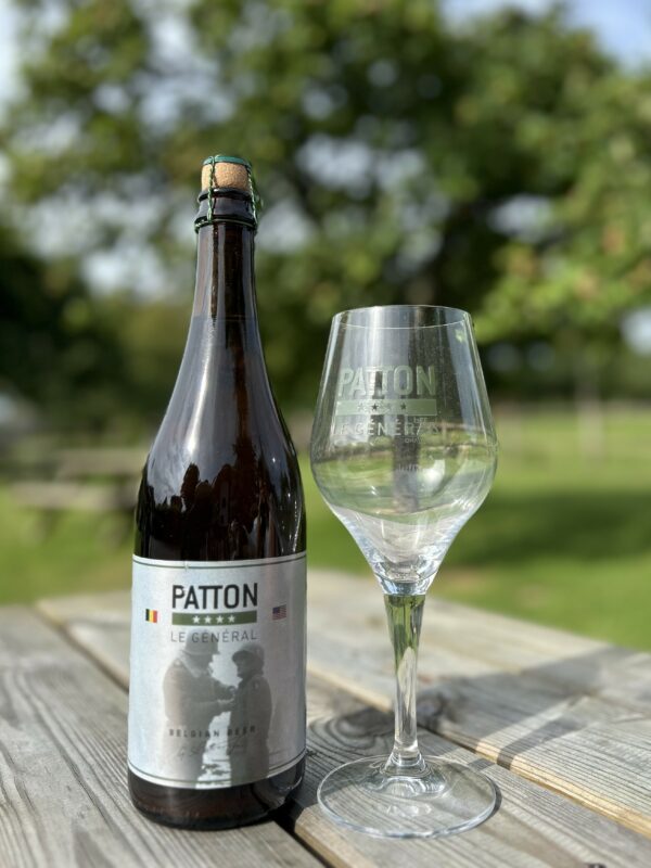 Bouteille de bière belge "Le Général" et un verre sur une table en bois, avec un arrière-plan naturel.