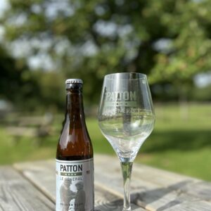 Bouteille de bière "PATTON Le Général" et verre sur une table en bois, avec un arrière-plan de verdure.