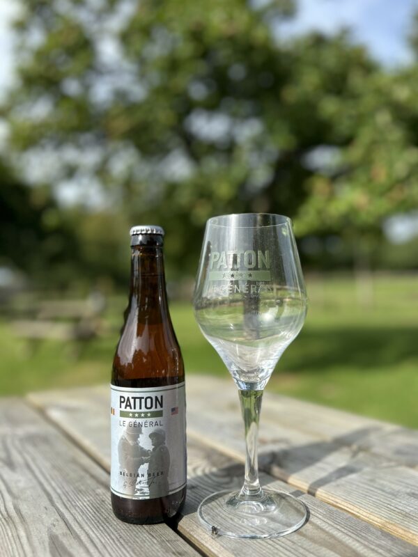 Bouteille de bière "PATTON Le Général" et verre sur une table en bois, avec un arrière-plan de verdure.
