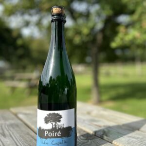 Bouteille de Poiré de la Cidrerie-Distillerie Théo Capelle sur une table en bois, en arrière-plan flou de verdure.
