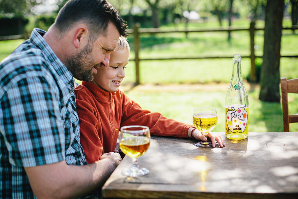 Théo Capelle et son fils partagent un moment convivial autour d'un verre de cidre sur une table en plein air.