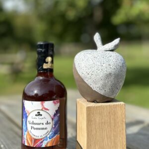 Bouteille de Velours de Pomme de la cidrerie Théo Capelle, accompagnée d'une sculpture en forme de pomme sur socle en bois.