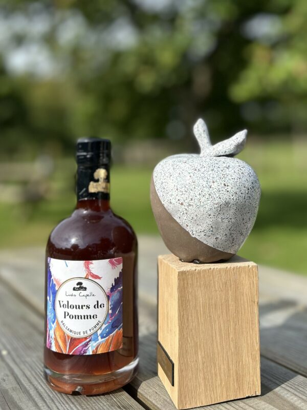 Bouteille de Velours de Pomme de la cidrerie Théo Capelle, accompagnée d'une sculpture en forme de pomme sur socle en bois.
